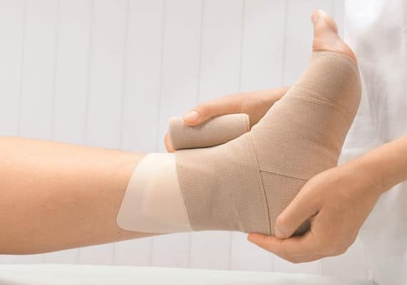 imagem mostra mão de enfermeira aplicando bandagem em ferida no tornozelo